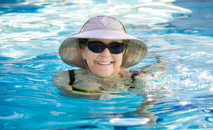 Senior woman wearing a hat and sunglasses in a swimming pool